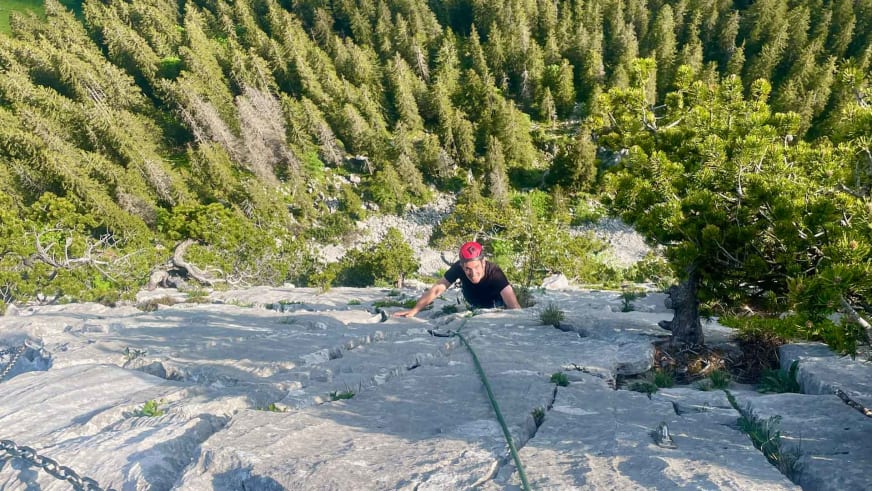 Bergwanderführer Alexander Hoffmann - Kuhnt klettert mit roter Kappe an einer steilen Kalksteinwand mit grünem Seil.