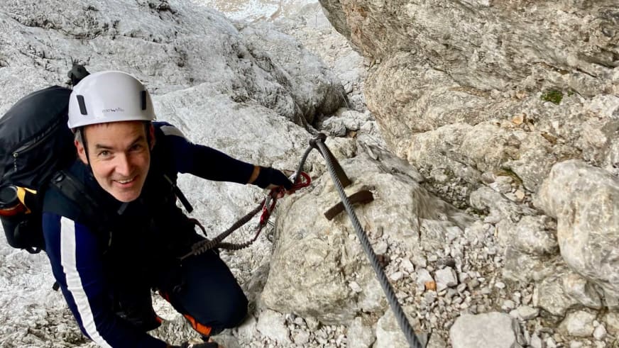 Bergwanderführer Alexander Hoffmann - Kuhnt am Klettersteig in Kalkstein mit weißem Helm und sichert sich am Drahtseil mit Karabinern.