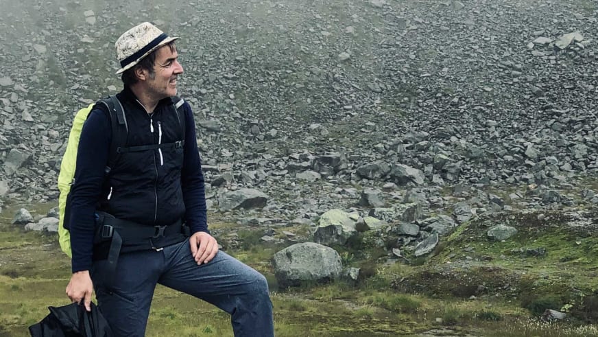 Bergwanderführer Alexander Hoffmann - Kuhnt mit hellem Hut sitzt lächelnd auf Felsblock in alpiner Gerölllandschaft.