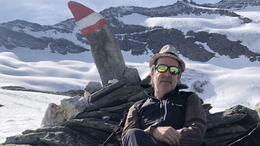 In Winterkleidung sitzt Bergwanderführer Alexander Hoffmann - Kuhnt auf Felsblöcken vor schneebedeckter Berglandschaft.