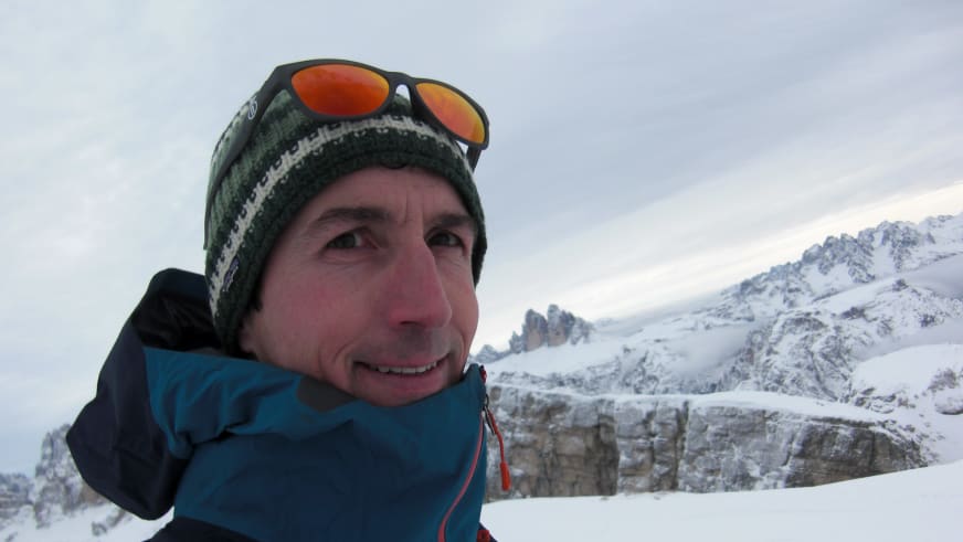 Portrait der Bergführerin Matthias Larcher mit grüner Wollmütze und Bergsteigerbrille vor schneebedeckten Gipfeln im Winter.