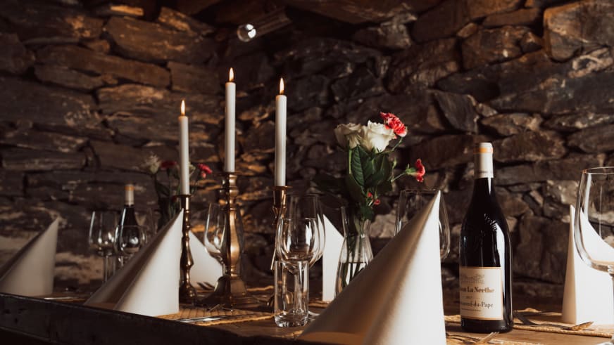 Elegant gedeckter Esstisch im Nes Gard Restaurant mit Kerzen, Rosen und Natursteinwand im Hintergrund.