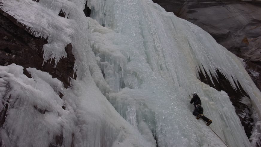 An vereister Felswand klettert Bergführerin Matthias Larcher mit Eisgeräten zwischen dicken Eiszapfen und gefrorenen Wasserfällen.