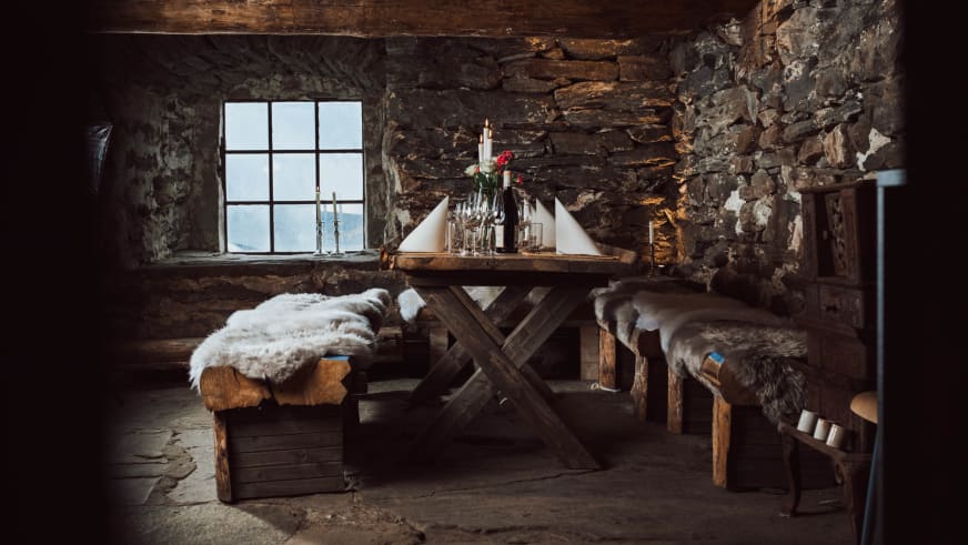 Rustikaler Speisesaal im Nes Gard mit Holztisch, Steinwänden und gemütlicher Kerzenbeleichtung.