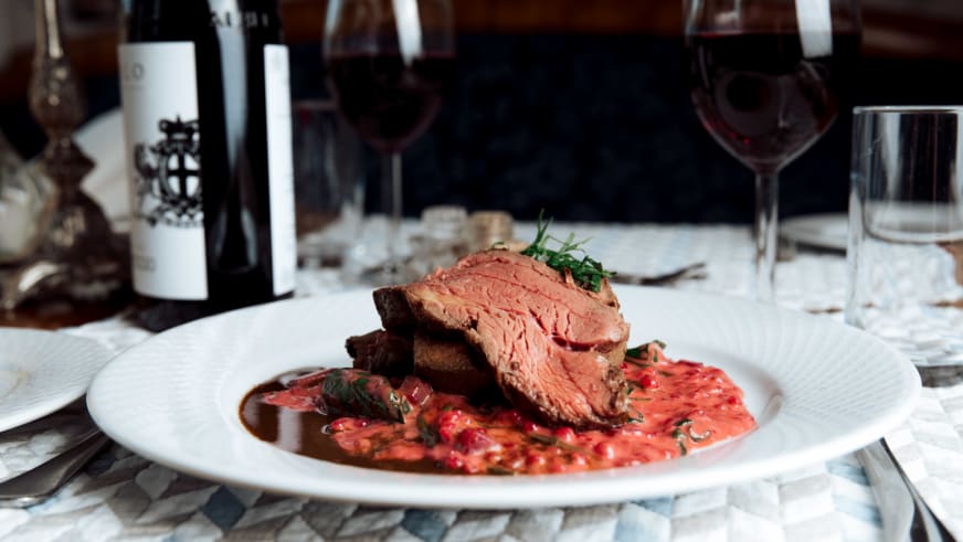 Rosa gebratenes Rindfleisch auf weißem Teller im Nes Gard Restaurant mit Rotwein und Kerzenschein.