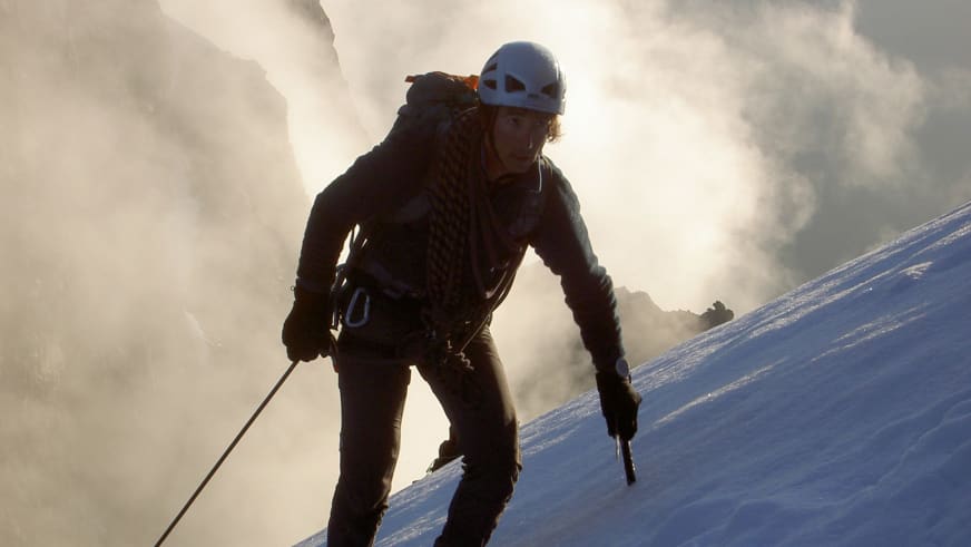Mit Eispickel und weißem Helm steigt Bergführerin Matthias Larcher den verschneiten Steilhang hinauf bei Hochtour im Gegenlichtn.