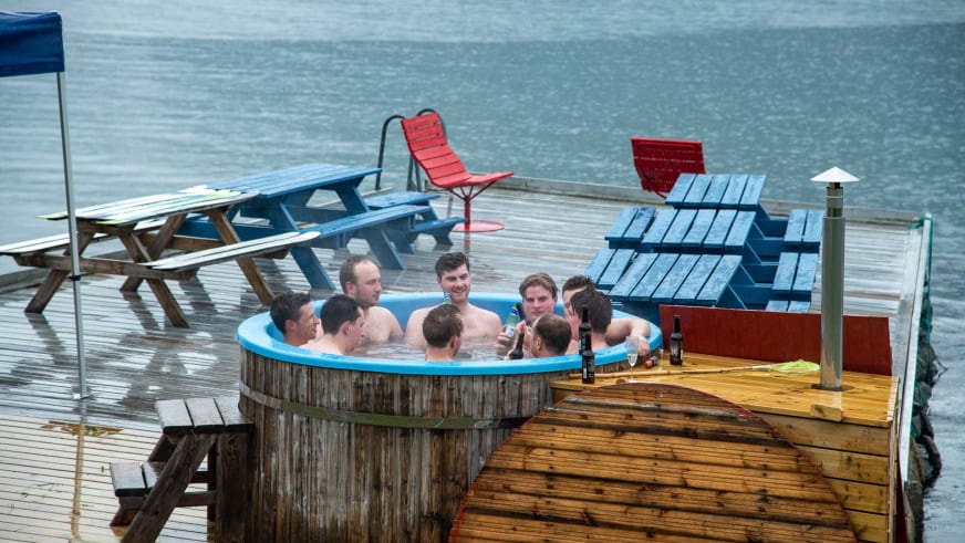 Gäste entspannen im Hot Tub auf der Holzterrasse vom Nes Gard direkt am Fjordufer.