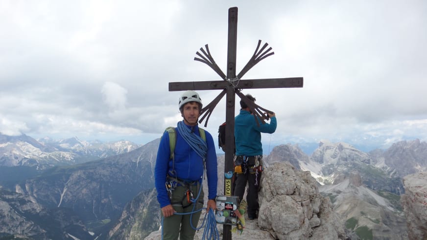 Bergführerin Matthias Larcher steht mit zweiter Person am hölzernen Gipfelkreuz nach erfolgreichem Kletteraufstieg am Kalksteingipfel.
