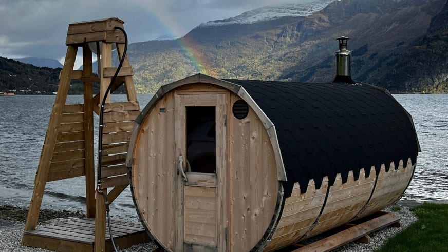 Mobile Fasssauna und Holz-Sprungturm am Ufer beim Nes Gard mit Fjordpanorama und Regenbogen.
