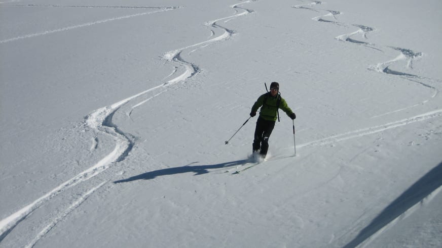 In grüner Skijacke fährt Bergführerin Matthias Larcher auf Skiern durch unverspurte Schneehänge bei sonnigem Wintertag.