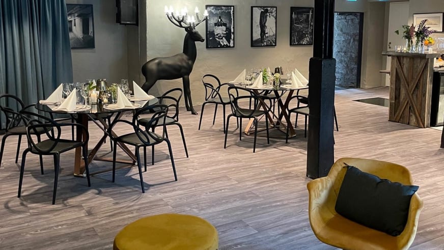 Moderner Restaurantbereich im Nes Gard mit runden Tischen, Designer-Stühlen und Hirschskulptur.