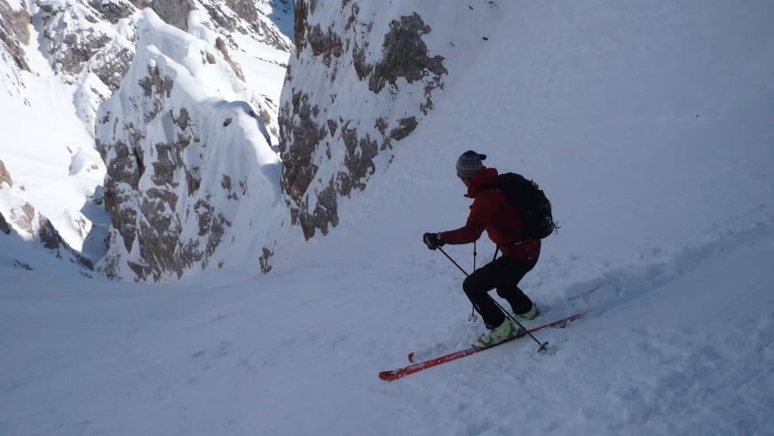 Auf Tourenskiern fährt Bergführerin Matthias Larcher den verschneiten Steilhang hinab zwischen schneebedeckten Felswänden im Hochgebirge.
