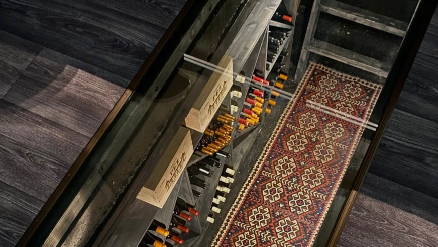 Blick von oben auf das Weinregal im Nes Gard Weinkeller mit verschiedenen Weinflaschen und Holzkisten.