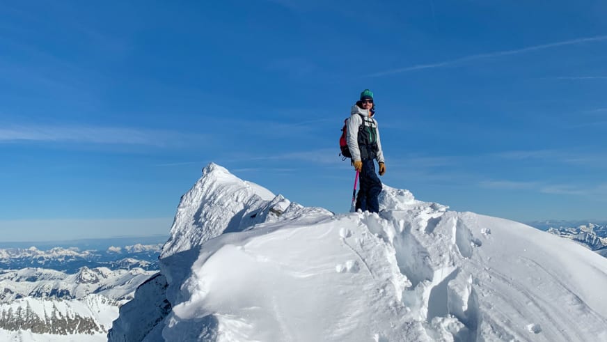 Bergführer Jakob Halder steht mit rosa Eispickel auf schneebedecktem Gipfel vor Hochgebirgskette.