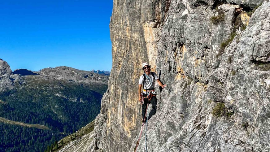 Bergführer Jakob Halder steht auf schmalem Felsband in steiler Kalksteinwand mit Klettergurt und rotem Seil.