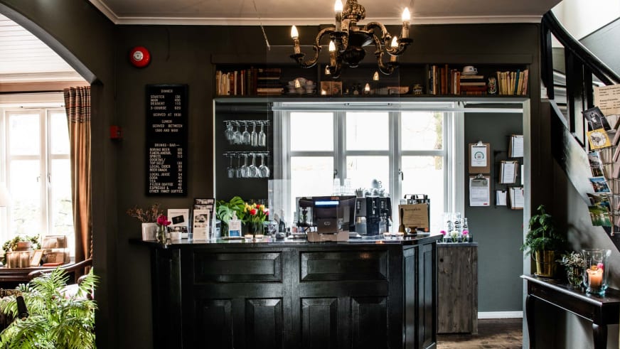 Rustikale Bar im Fjærland Fjordstove Hotell mit dunkler Holztheke und Messingkronleuchter.