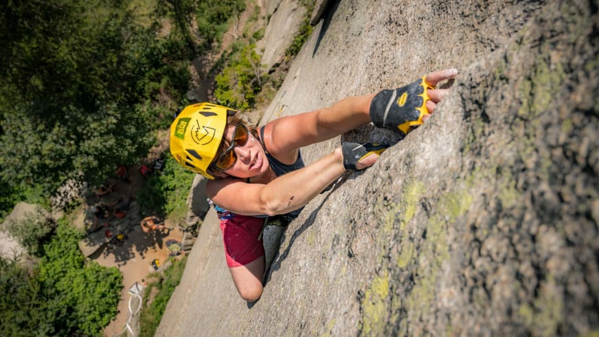 Mit gelbem Helm und Sonnenbrille klettert Bergführerin Tanja Kuster frei an senkrechter grauer Felswand.