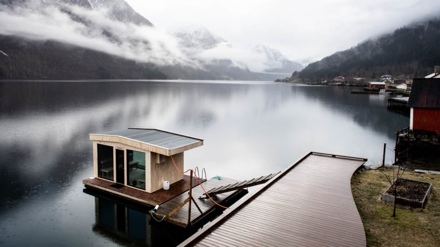 Schwimmende Sauna auf dem Sognefjord vor dem Fjærland Fjordstove Hotell mit Blick auf schneebedeckte Berge.
