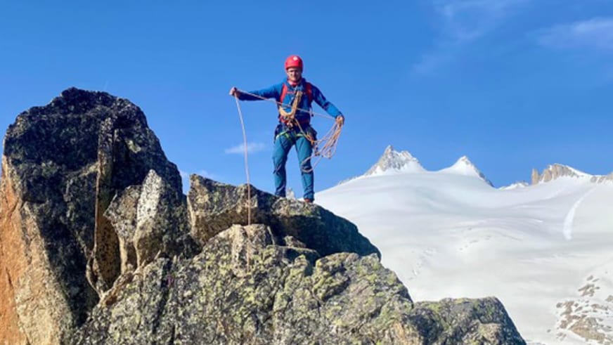 Bergführer Maurits Bakker steht mit Kletterseil auf einem schmalen Felsgrat vor schneebedeckten Gipfeln und Gletscherfeld.