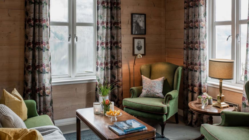 Gemütlicher Aufenthaltsraum im Fjærland Fjordstove Hotell mit bunten Sesseln und Blick auf die norwegische Berglandschaf