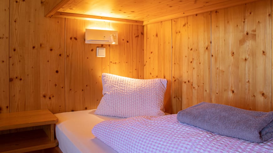 Schlafraum der Schihütte Zams mit komplett holzverkleideten Wänden und Einzelbett mit karierter Bettwäsche.