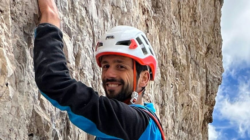 Bergführer Cesare Lotti lächelt mit weißem Petzl-Kletterhelm vor einer hellen Kalksteinwand.