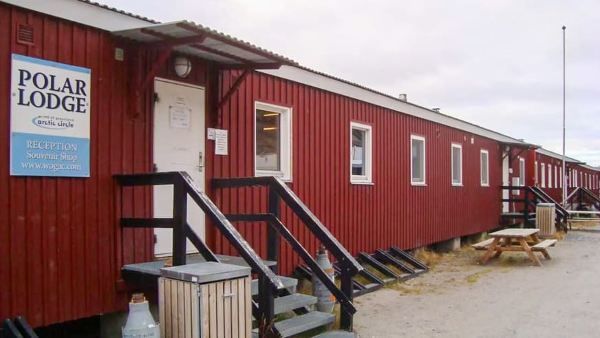 Außenansicht der Polar Lodge als langgestrecktes rotes Holzgebäude auf Stelzen mit weißen Fensterrahmen.