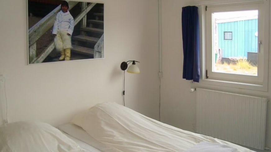 Gemütliches Gästezimmer in der Polar Lodge mit Einzelbett, weißer Bettwäsche und Wandleuchte.