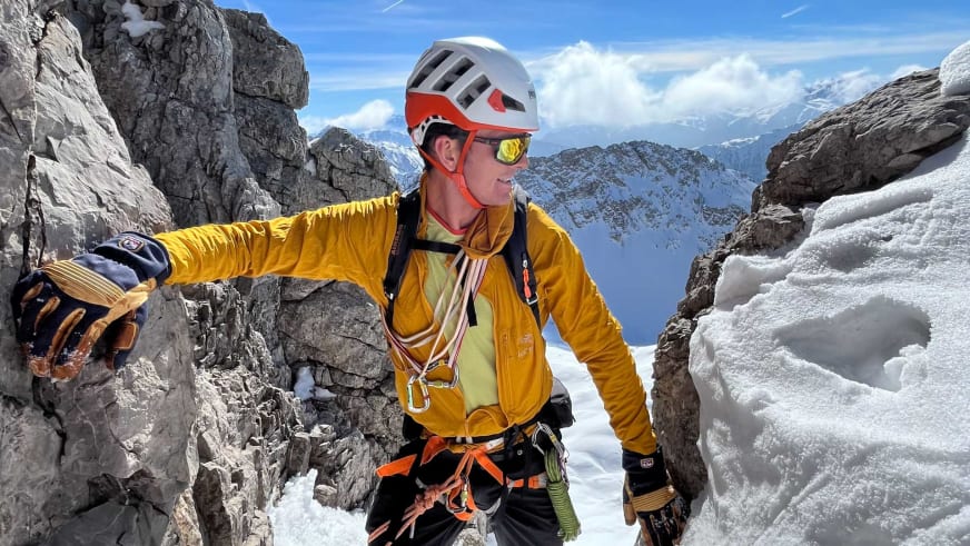 Bergwanderführer Patrick Hindelang klettert in gelber Softshell-Jacke an grauer Kalksteinwand mit weißem Helm und Klettergurt.