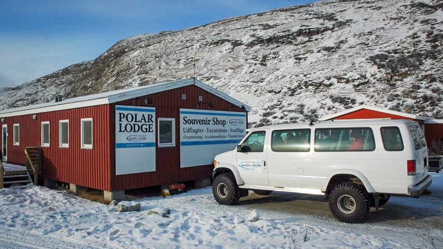 Winteransicht der Polar Lodge in verschneiter Landschaft mit weißem Geländewagen vor dem Eingang.