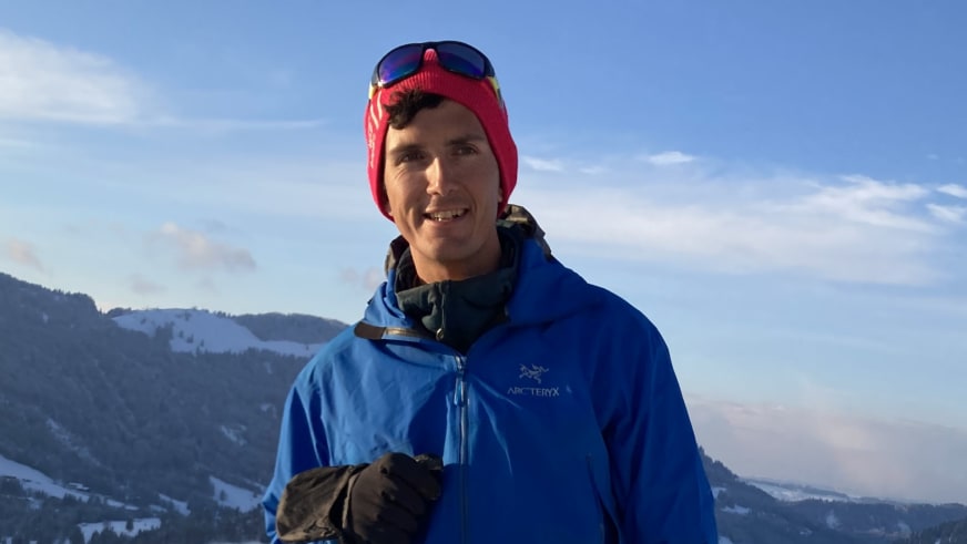 Bergwanderführer Patrick Hindelang mit roter Mütze und blauer Arc'teryx Jacke vor verschneiter Berglandschaft.
