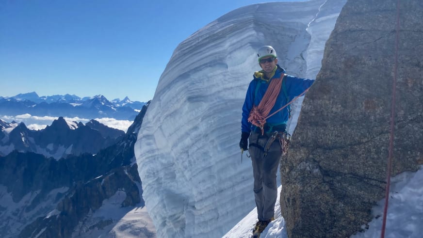Auf schmalem Firnrücken steht Bergwanderführer Patrick Hindelang mit blauer Jacke und weißem Bergsteigerhelm.