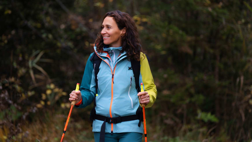 Corina Machon hält orange Wanderstöcke und trägt hellblaue Softshell-Jacke, Bergwanderführerin bei Bergtour.