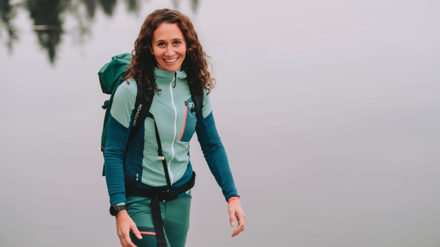 Corina Machon geht in grüner Outdoorkleidung und grünem Rucksack, Bergwanderführerin in natürlicher Bewegung.