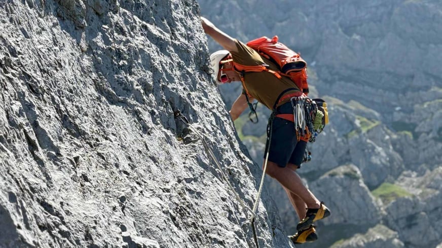 Bergführer Robert Kadner klettert in roter Kleidung an einer steilen grauen Felswand mit Kletterausrüstung am Gurt.