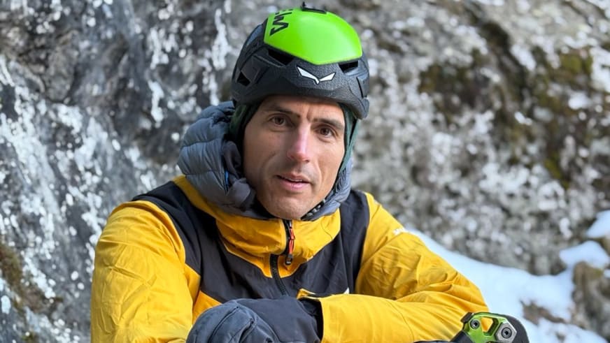 Bergführerin Luca Trubbiani lächelt in die Kamera und trägt grün-schwarzen Kletterhelm und gelbe Daunenjacke.