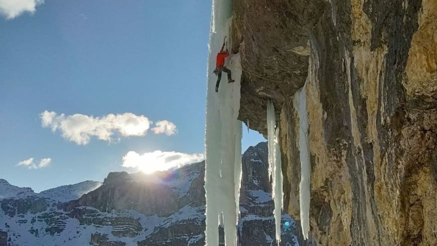 An einer senkrechten Eiswand mit dicken Eiszapfen klettert Bergführerin Luca Trubbiani in roter Winterjacke.