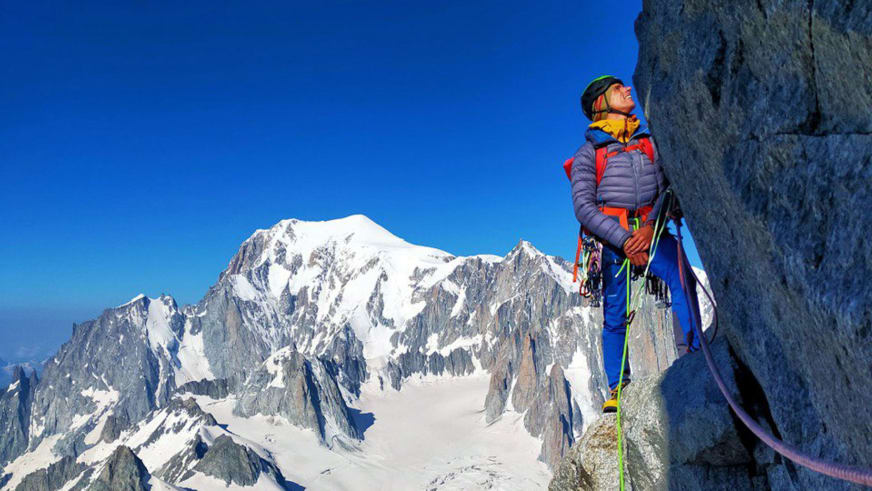 Bergführerin Luca Trubbiani in bunter Winterkleidung steht am Fels und blickt nach oben zum Himmel.