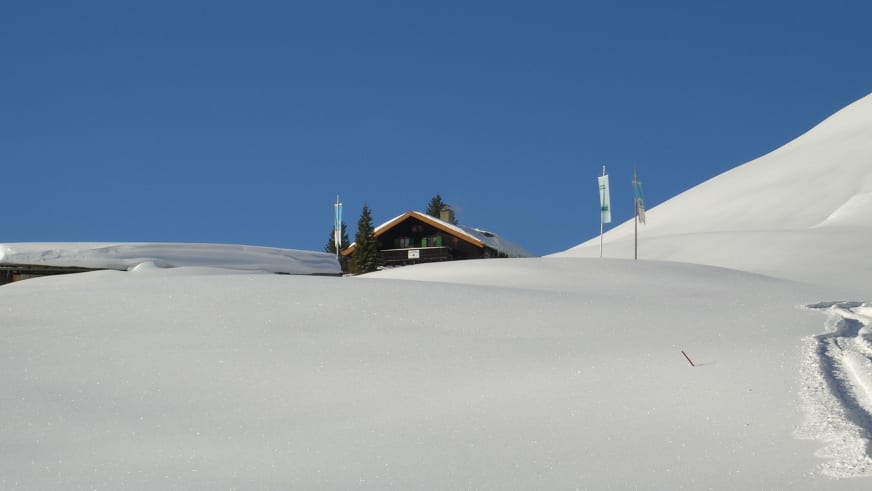 Winterpanorama der Schönfeldhütte zwischen hohen Schneewehen unter blauem Himmel in alpiner Lage.
