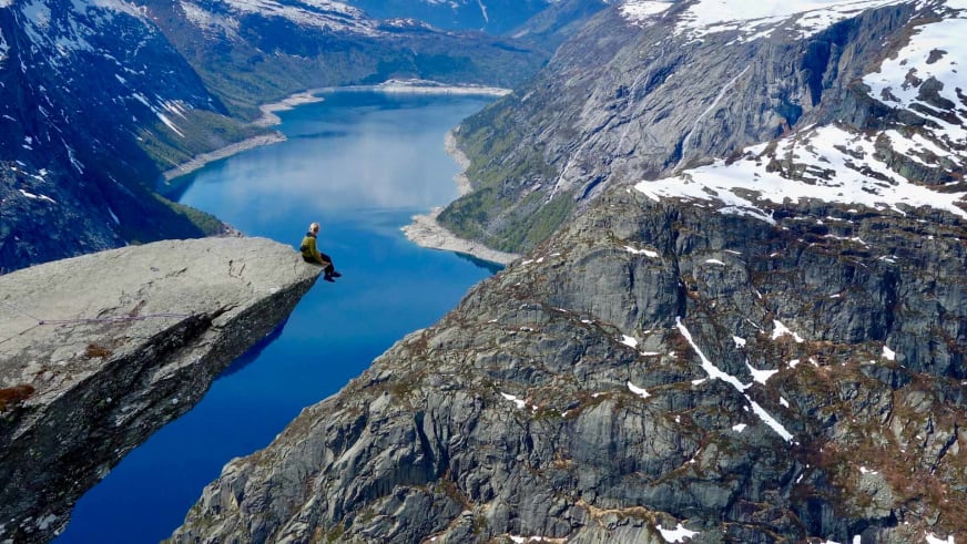 Bergwanderführerin Nora Coenen in gelber Jacke sitzt auf einem Felsvorsprung und blickt hinunter auf den tiefblauen Fjord.