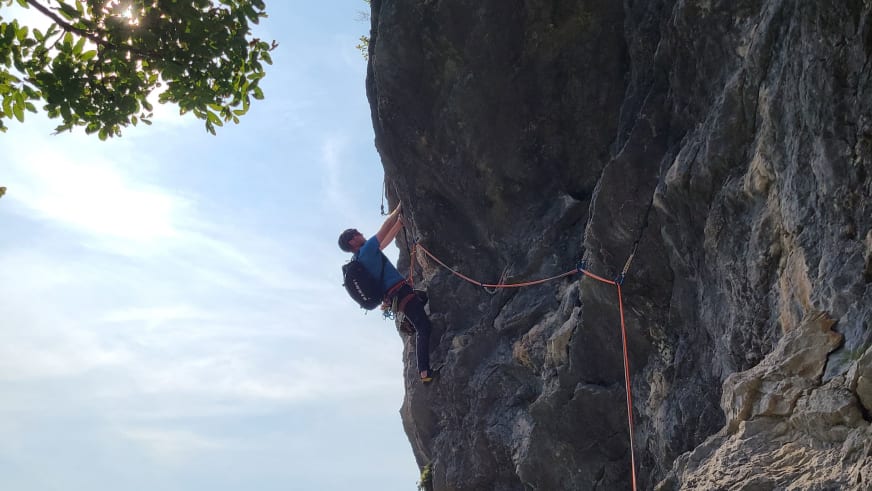 An grauer Kalksteinwand klettert Bergführer Lukas Degen mit blauem Oberteil und orangefarbenem Seil.