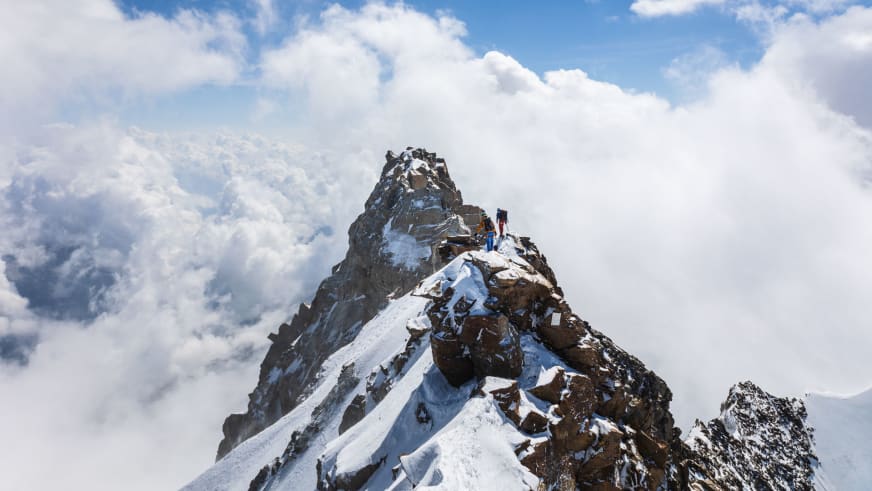 Bergwanderführer Jonas Bergmann mit zweiter Person am schmalen Gipfelgrat eines steilen, schneebedeckten Felsgipfels.