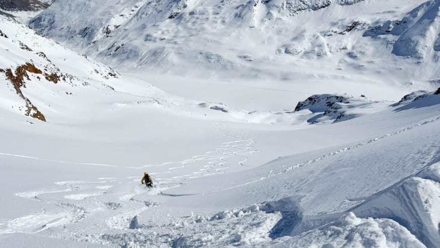 In gelber Jacke fährt Bergführer Alexander Brückler durch Pulverschnee und wirbelt dabei eine Schneewolke auf.