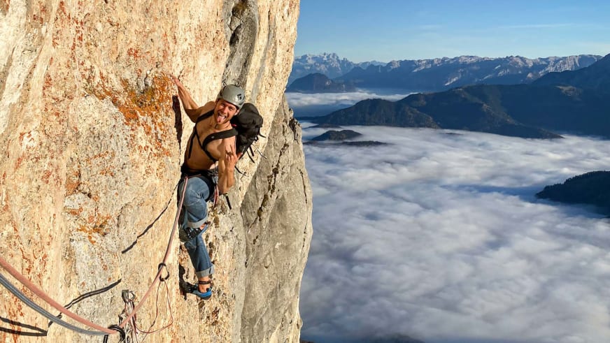 In steiler Kalksteinwand klettert Bergführer Alexander Brückler mit grauem Helm und blauer Kletterhose am Seil gesichert.