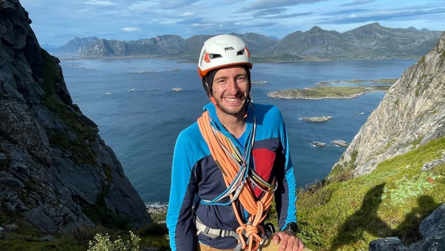 Portrait von Bergführer Christoph Blumrich mit weißem Helm vor weitläufiger Fjordlandschaft mit blauen Gewässern.