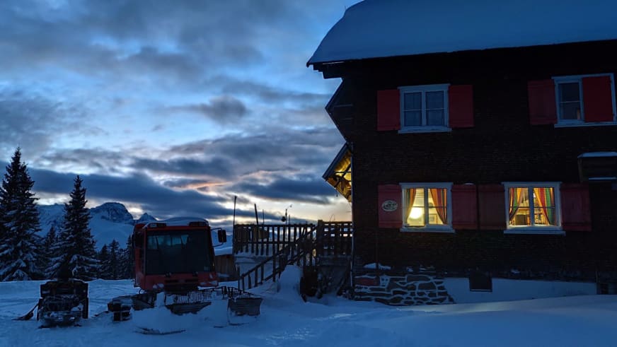 Winterliche Dämmerung am Neuhornbachhaus mit warm erleuchteten Fenstern und schneebedeckter Bergkulisse.