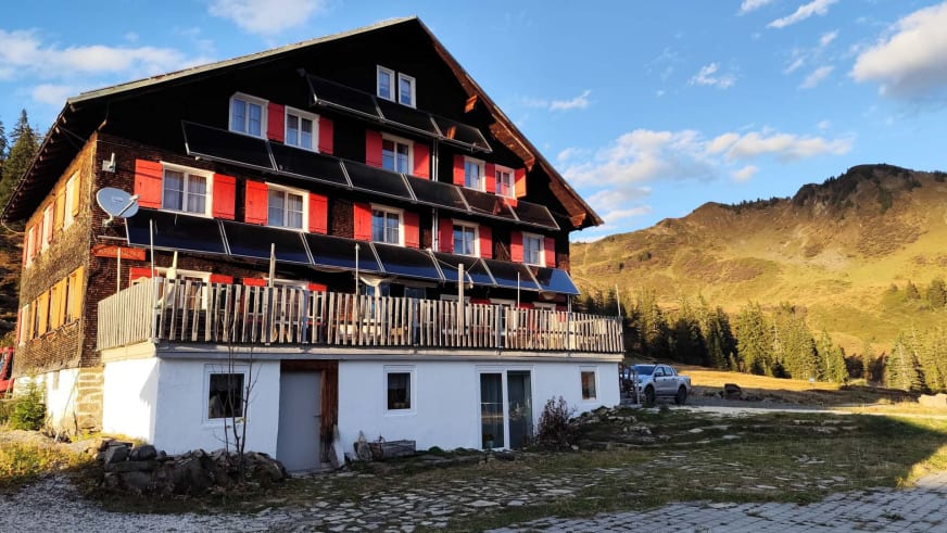 Sommeraufnahme des Neuhornbachhaus mit charakteristischem Holzbalkon und bewaldeten Berghängen im Hintergrund.