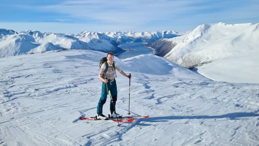 Bergwanderführerin Magdalena Strötz steht auf roten Tourenski in einer Schneelandschaft mit Fjord und Bergen im Hintergrund.