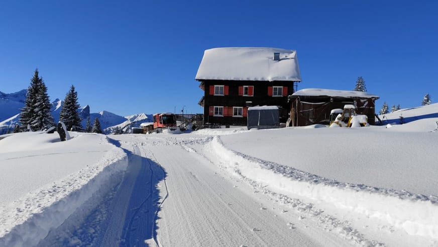 Winterpanorama des Neuhornbachhaus mit geräumter Zufahrtsstraße und schneebedeckter Bergkette im Hintergrund.