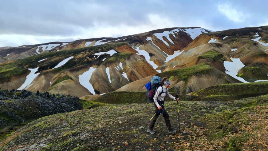 Mit Wanderstöcken und Rucksack wandert Bergwanderführerin Magdalena Strötz über moosbewachsene Hänge zwischen Braun- und Beigetönen.